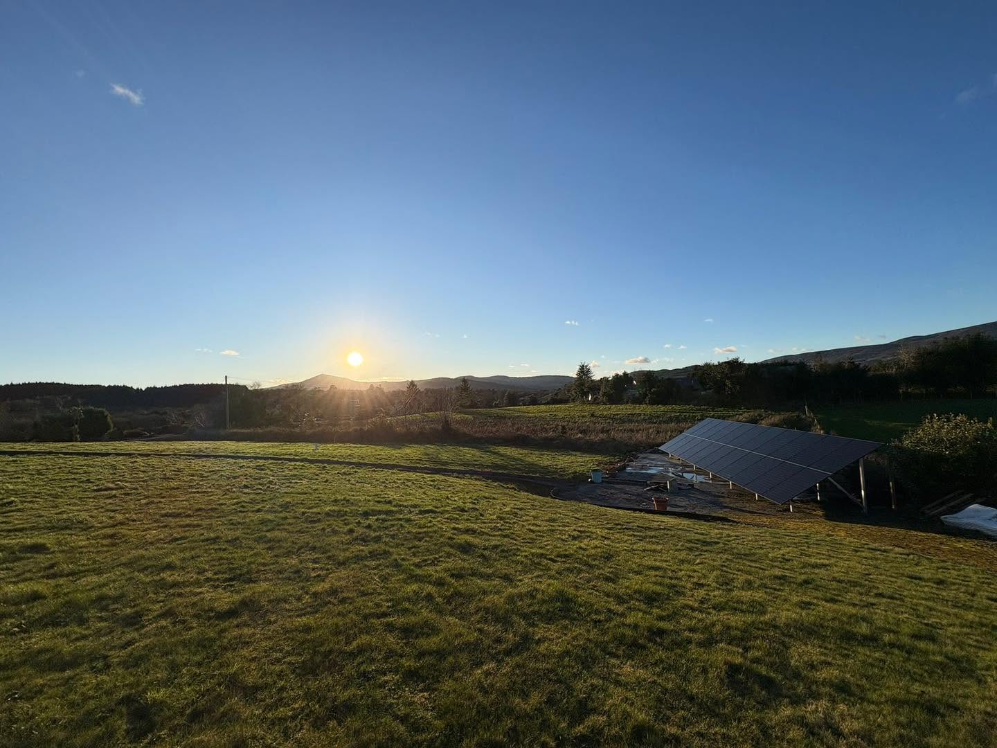 Solar panels installed on a farm in Cork, Ireland, with fields and sunset in the background.